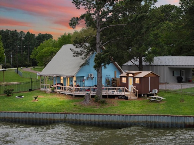 back of property at dusk featuring an outbuilding, a deck with water view, fence, and a lawn