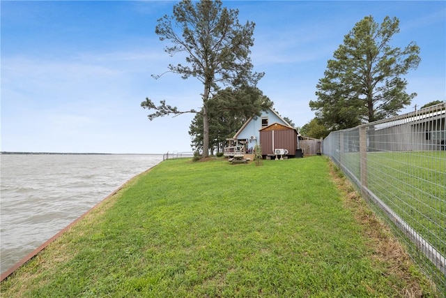 view of yard featuring a water view, an outdoor structure, fence, and a storage unit