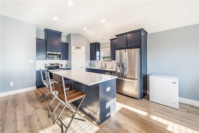 kitchen featuring appliances with stainless steel finishes, light wood-type flooring, vaulted ceiling, sink, and a center island