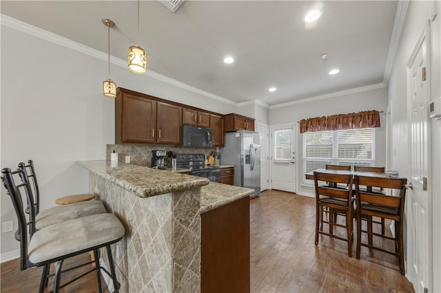 kitchen with kitchen peninsula, crown molding, decorative light fixtures, a breakfast bar area, and black appliances