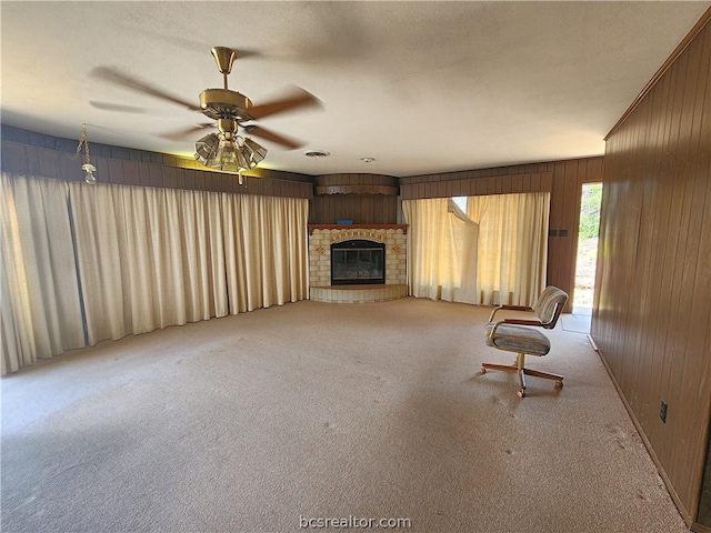 unfurnished room featuring ceiling fan, light colored carpet, wooden walls, and a brick fireplace