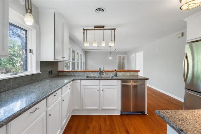 3907 Nagle St N, Bryan, TX 77801 - kitchen with appliances with stainless steel finishes, dark wood-type flooring, a peninsula, white cabinets, and hanging light fixtures