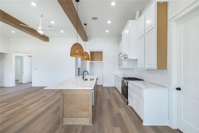 kitchen featuring white cabinets, an island with sink, beamed ceiling, and gas range