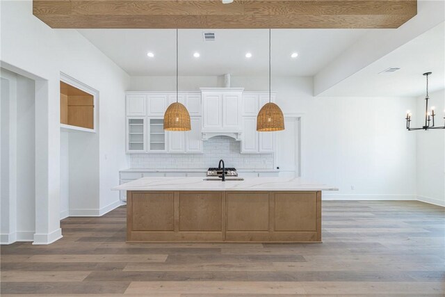 kitchen featuring white cabinetry, light stone countertops, a large island with sink, hardwood / wood-style floors, and decorative light fixtures