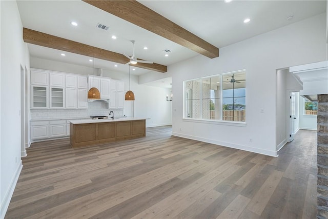 kitchen with white cabinetry, beamed ceiling, backsplash, hardwood / wood-style floors, and a center island with sink