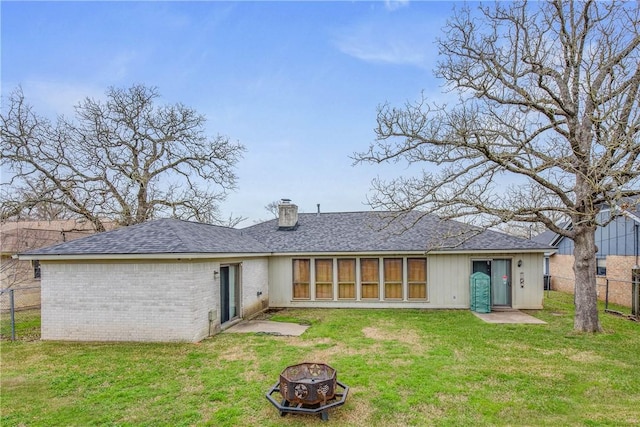 back of property with an outdoor fire pit, a chimney, fence, a yard, and brick siding