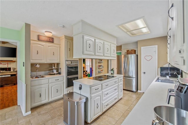 kitchen with a kitchen island, a sink, white cabinetry, light countertops, and black appliances