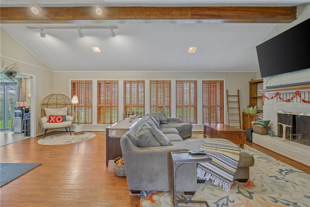 living room with vaulted ceiling with beams, a brick fireplace, and light wood-style flooring