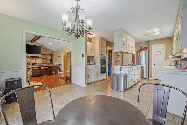 dining room with vaulted ceiling with beams, a wainscoted wall, light tile patterned floors, and a chandelier