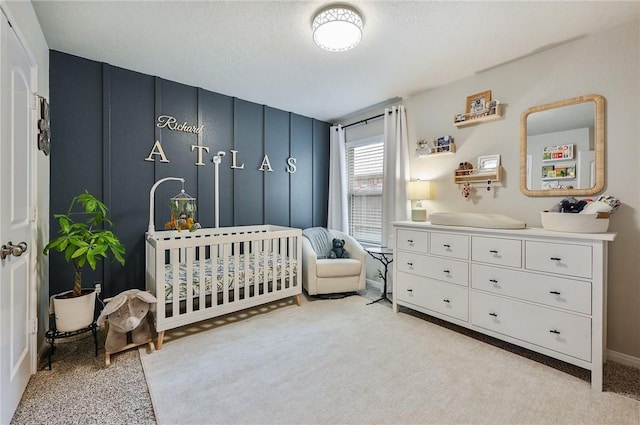 bedroom featuring a crib, a textured ceiling, and light colored carpet