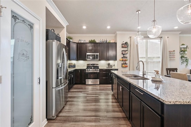 kitchen with pendant lighting, sink, ornamental molding, appliances with stainless steel finishes, and wood-type flooring