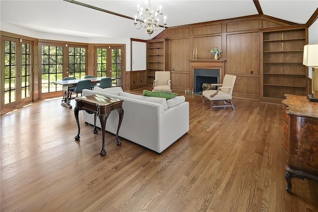 living room featuring french doors, wooden walls, wood-type flooring, a notable chandelier, and lofted ceiling