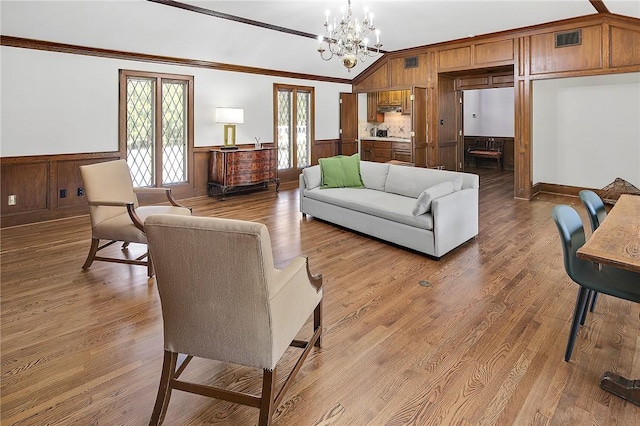 living room with a notable chandelier, crown molding, hardwood / wood-style floors, wood walls, and vaulted ceiling