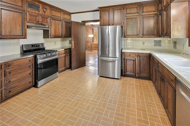 kitchen with backsplash, sink, stainless steel appliances, and ornamental molding