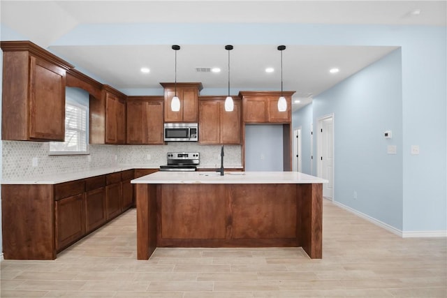 kitchen with pendant lighting, sink, stainless steel appliances, and an island with sink