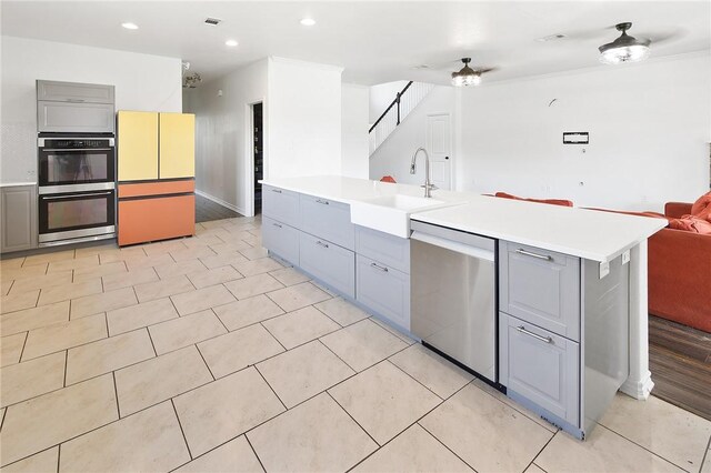 kitchen with a center island with sink, sink, ceiling fan, gray cabinets, and appliances with stainless steel finishes