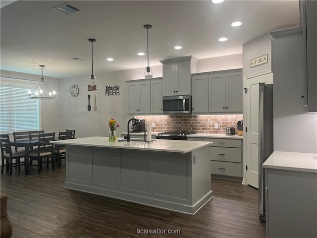 kitchen with a kitchen island with sink, sink, hanging light fixtures, a notable chandelier, and dark hardwood / wood-style flooring