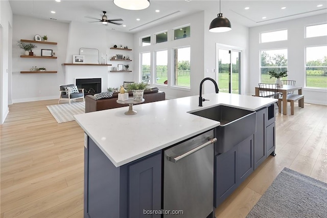 kitchen featuring hanging light fixtures, an island with sink, stainless steel dishwasher, and light wood-type flooring