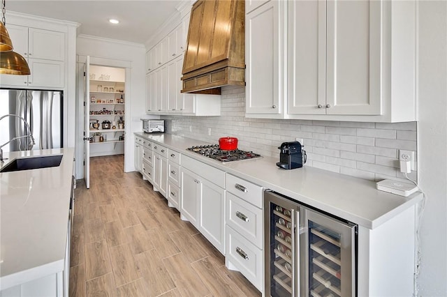 kitchen with wine cooler, light countertops, appliances with stainless steel finishes, white cabinets, and premium range hood