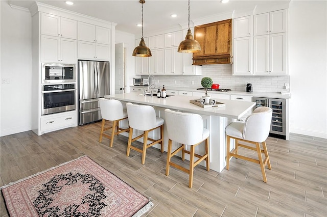 kitchen with appliances with stainless steel finishes, beverage cooler, light countertops, and white cabinetry