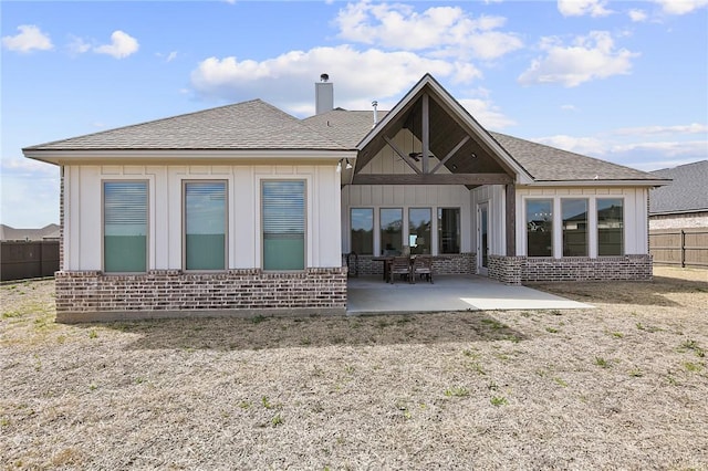 back of house with board and batten siding, brick siding, a patio, and fence