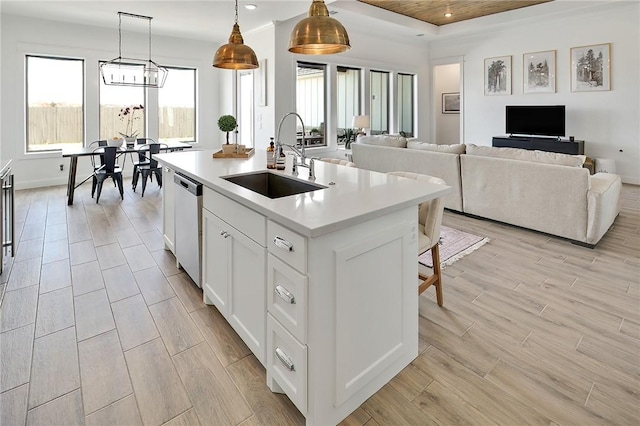 kitchen with a center island with sink, hanging light fixtures, open floor plan, white cabinets, and a sink