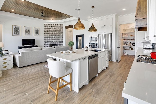 kitchen with stainless steel appliances, a kitchen island with sink, white cabinetry, and light countertops