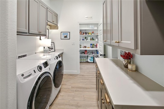 clothes washing area with light wood-type flooring, washing machine and clothes dryer, cabinet space, and baseboards