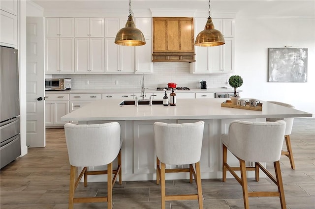 kitchen with white cabinets, an island with sink, decorative light fixtures, light countertops, and premium range hood