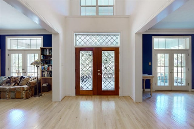 entrance foyer with french doors, a towering ceiling, and light wood-type flooring