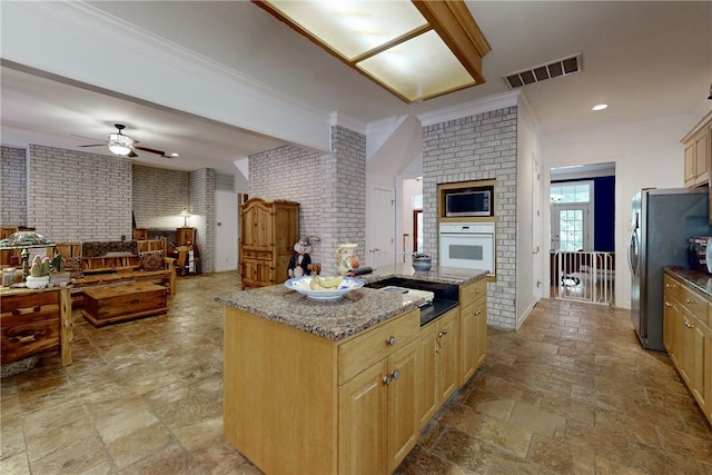 kitchen with light brown cabinetry, light stone counters, brick wall, stainless steel appliances, and a kitchen island