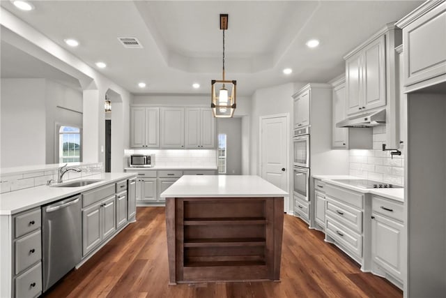 kitchen with decorative light fixtures, a tray ceiling, backsplash, appliances with stainless steel finishes, and sink