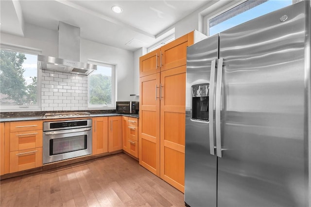 213 N Houston Ave, Bryan, TX 77803 - kitchen with stainless steel appliances, wall chimney exhaust hood, dark countertops, light wood-style flooring, and healthy amount of natural light