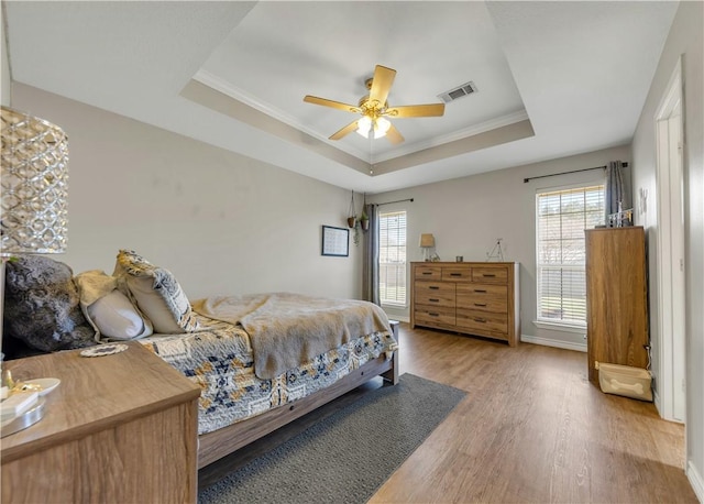 bedroom featuring wood finished floors, multiple windows, a raised ceiling, and visible vents