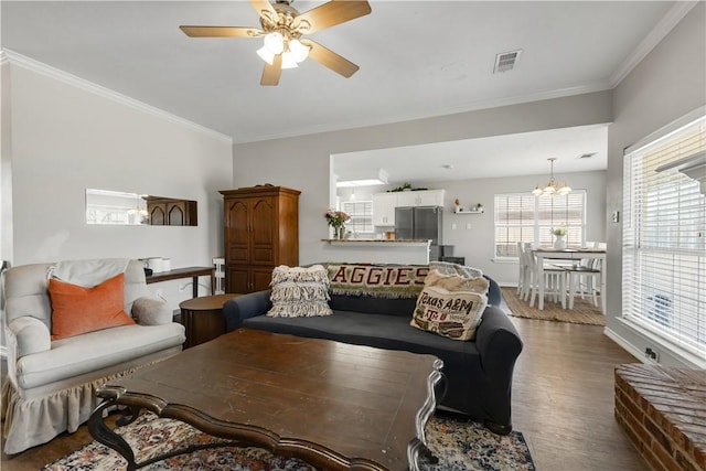 living room with ceiling fan with notable chandelier, wood finished floors, visible vents, baseboards, and ornamental molding