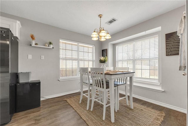 dining room with a notable chandelier, baseboards, visible vents, and wood finished floors