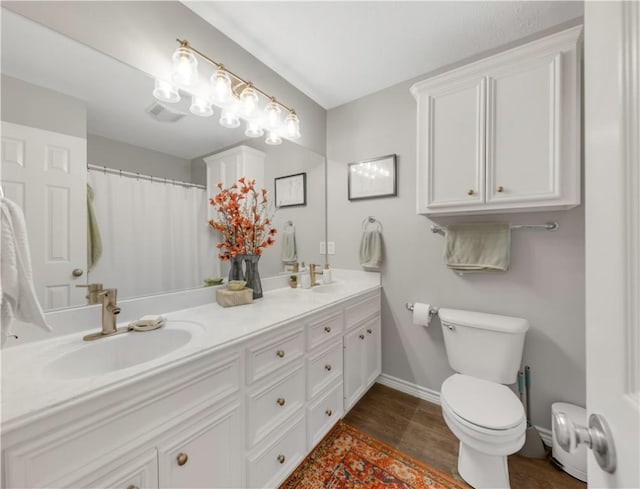 bathroom featuring toilet, wood finished floors, a sink, baseboards, and double vanity