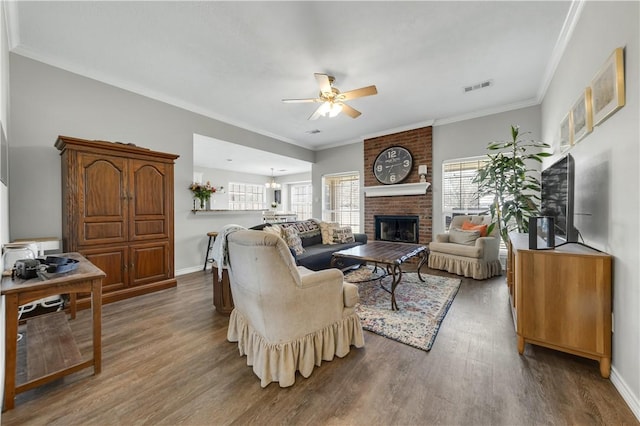 living room featuring a brick fireplace, baseboards, visible vents, and wood finished floors