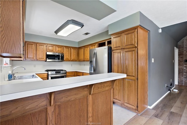 2811 Arroyo Ct N, College Station, TX 77845 - kitchen featuring appliances with stainless steel finishes, a sink, light countertops, a peninsula, and light wood finished floors