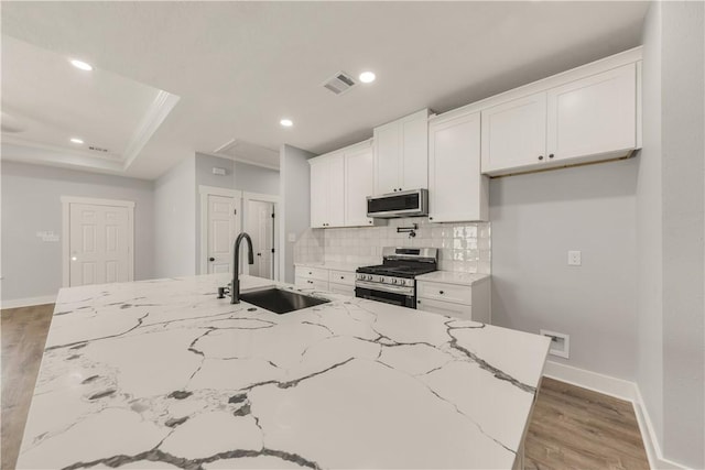 kitchen with white cabinetry, sink, stainless steel appliances, and a center island with sink