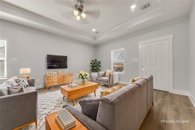 living room featuring hardwood / wood-style flooring, ornamental molding, a raised ceiling, and ceiling fan