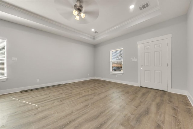 empty room with crown molding, a tray ceiling, and light wood-type flooring