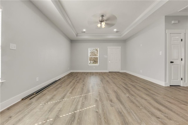 empty room featuring a tray ceiling, ornamental molding, ceiling fan, and light wood-type flooring