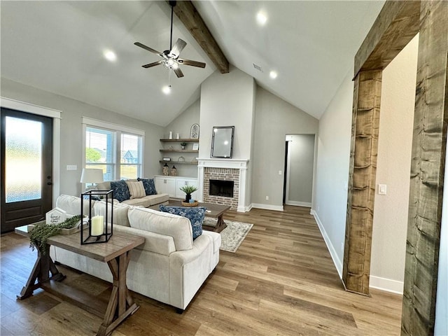 living room featuring lofted ceiling with beams, ceiling fan, light hardwood / wood-style floors, and a brick fireplace