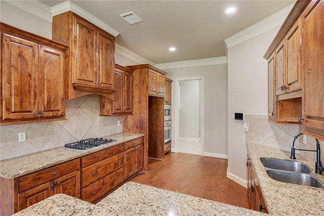 15613 Wood Brook Ln, College Station, TX 77845 - kitchen with appliances with stainless steel finishes, light stone countertops, wood finished floors, decorative backsplash, and crown molding