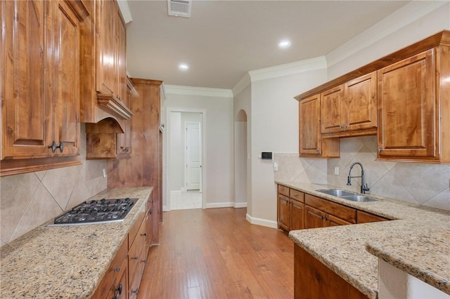 15613 Wood Brook Ln, College Station, TX 77845 - kitchen with stainless steel gas stovetop, arched walkways, brown cabinets, light stone countertops, and ornamental molding