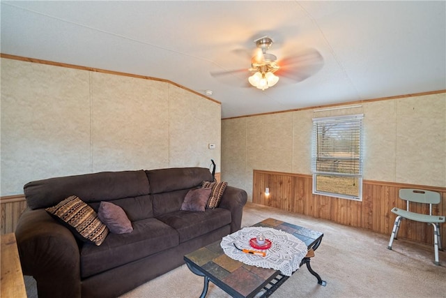 living room with a wainscoted wall, a ceiling fan, crown molding, and carpet