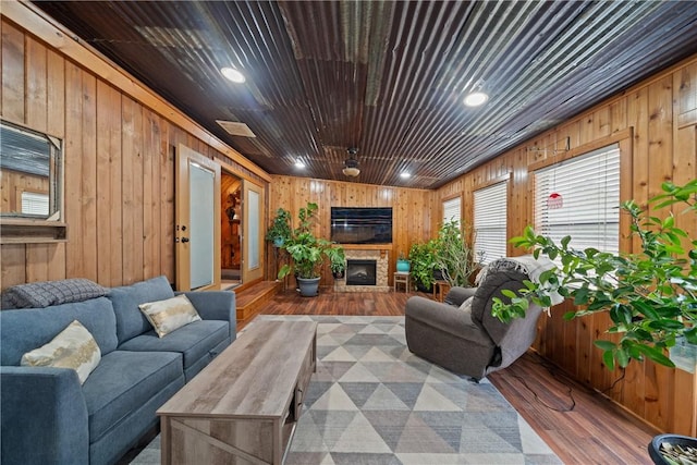 living room with wood finished floors, wooden walls, a fireplace with raised hearth, and wooden ceiling