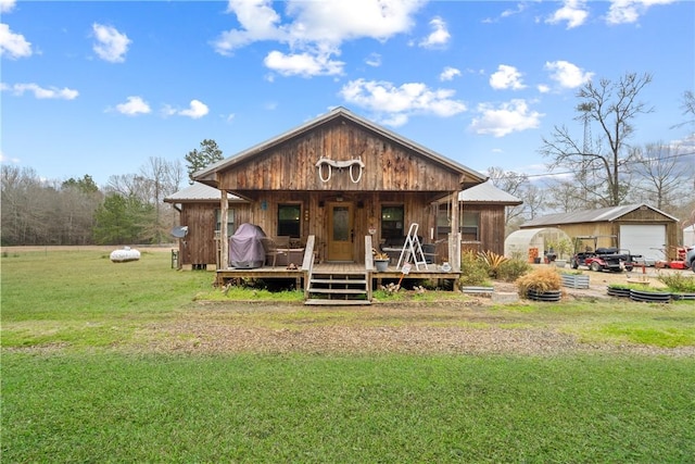 back of property featuring a porch, an outdoor structure, a garage, a lawn, and metal roof