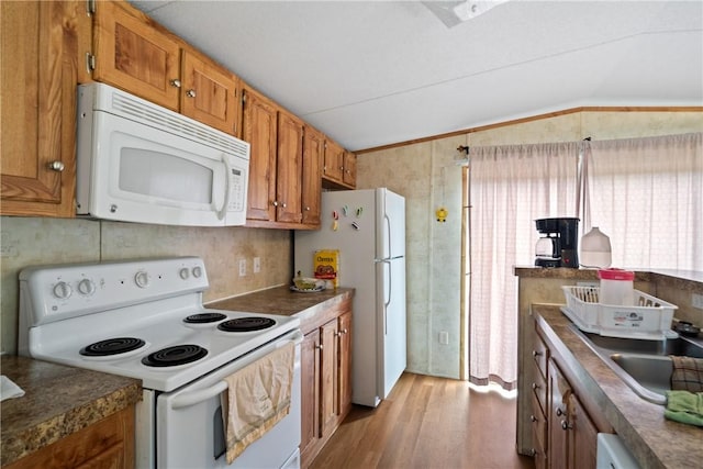 kitchen with brown cabinetry, white appliances, and vaulted ceiling